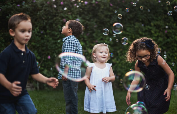 Bambini che giocano con le bolle di sapone in giardino con un'educatrice